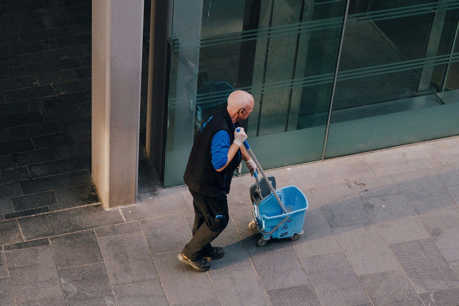 A cleaner moving a mop bucket outside a commercial building